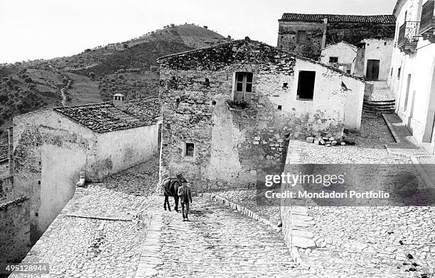 Suggestive view of the village of Rocca Imperiale with the hills on the background; a boy with a donkey is climbing the steep road going to the...