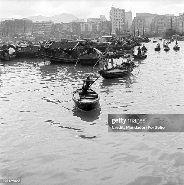 Some people moving by their rowing boats in the Aberdeen Harbour. In the background, many junks are moored. Junks are the boats used by Chinese...