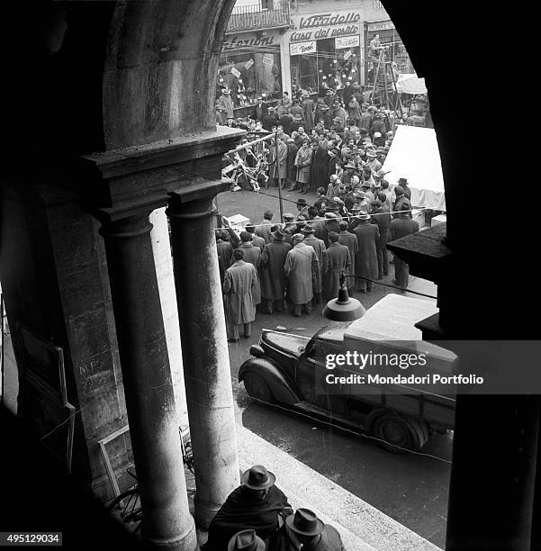 Crowd of people in the street is visible from an arcade. Vicenza, 1955