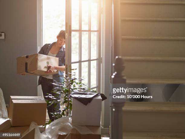 and woman carrying a packing box into her new home - moving house stock pictures, royalty-free photos & images