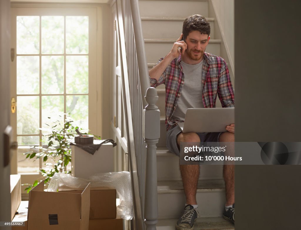 A man moving house working on phone and laptop
