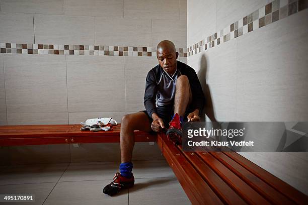 football goal keeper tying shoes in changing room - football bench stock pictures, royalty-free photos & images