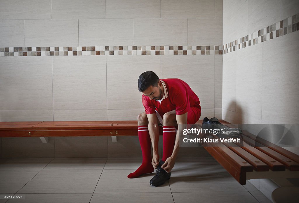 Football player tying shoe, alone in changing room