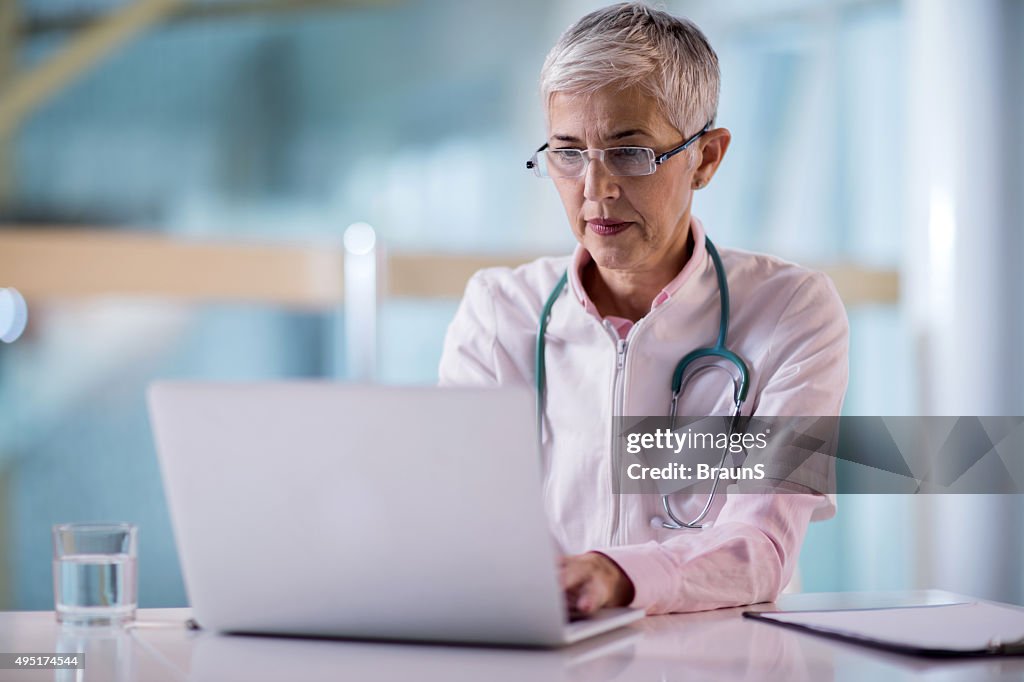 Mature female doctor working on laptop in the office.