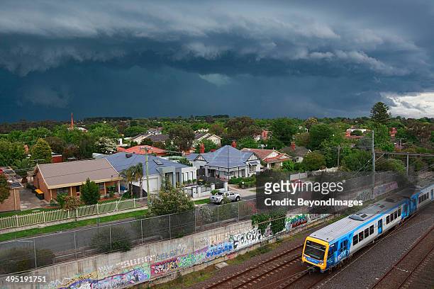 dark, threatening storm looms over suburbs with metro train - melbourne train stock pictures, royalty-free photos & images
