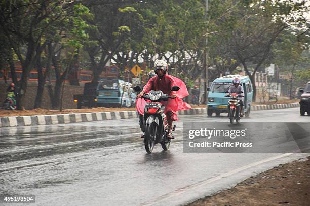 Motorcycle rider wearing a poncho to cover himself from the rain. Heavy rain hit the city after four dry months.