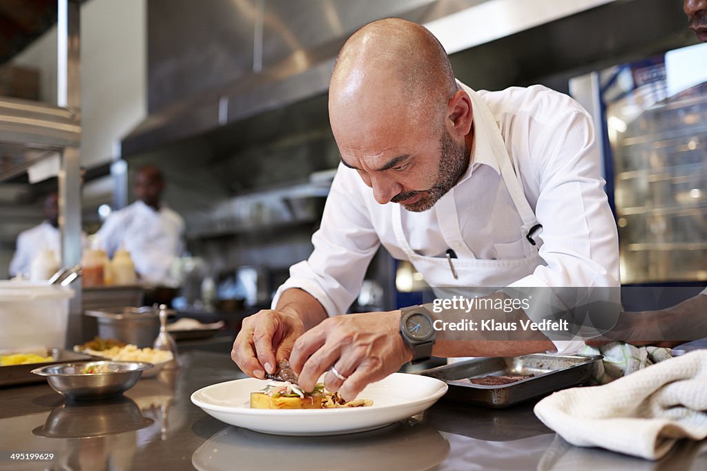 Head chef finishing dish in kitchen at restaurant
