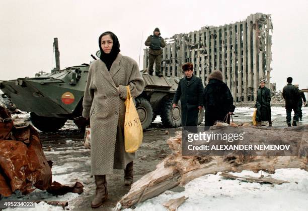 Chechen women and men pass in February 1996 by a Russian Army armoured personnel carrier in front of destroyed presidential palace in Grozny, capital...