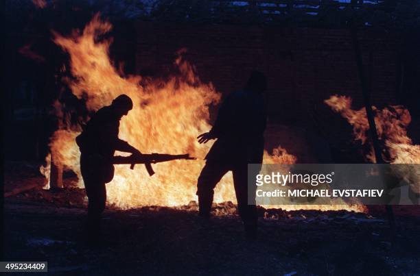 Two Chechen fighters warm by the fire burning next to a house destroyed by Russian artillery in the center of Grozny, 15 January 1995. Russian troops...