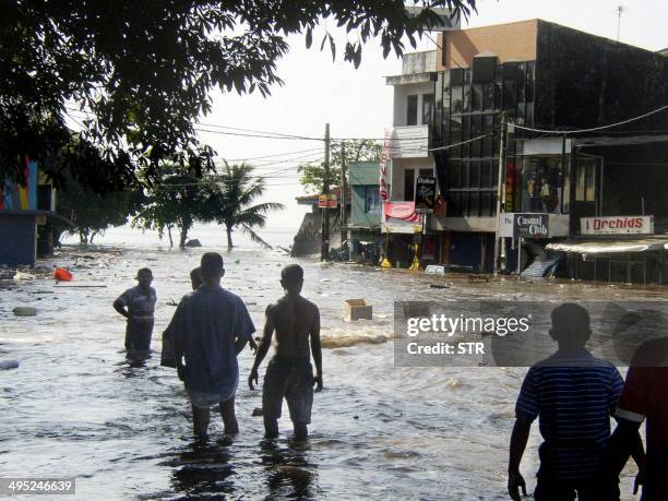 In this picture taken 26 December 2004, Sri Lankan pedestrians walk through floodwaters in a main street of Galle, after the coastal town was hit by...
