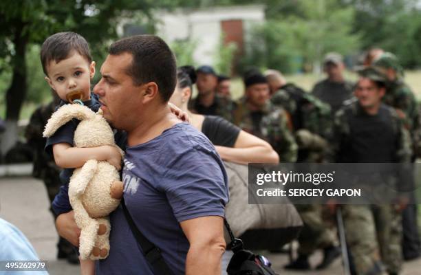 Man carries his son as he leaves his apartment building during an ongoing shoot-out between pro-Russia militants and border guards defending the...