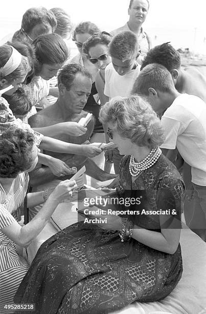 American actor Henry Fonda signing autographs at Lido di Venezia, during the Film Festival. Beside him, his wife Afdera Franchetti. Venice, 1957