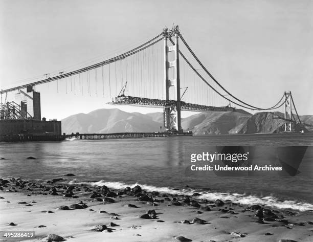 View from Crissy Field in the Presidio of the construction of the Golden Gate Bridge with the roadbed being installed, San Francisco, California,...