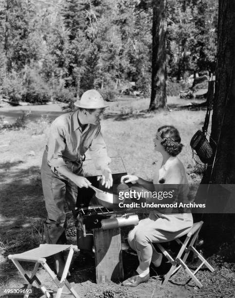 Actors William Powell and Myrna Loy at a cook stove while camping in a scene from a movie, Hollywood, California, circa 1935.