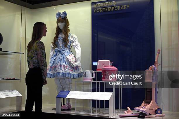 Member of staff poses next to a display featuring a doll titled 'Sweet Ensemble by Baby, the Stars Shine Bright' dating from 2011-12 and a Hello...