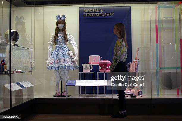 Member of staff poses next to a display featuring a doll titled 'Sweet Ensemble by Baby, the Stars Shine Bright' dating from 2011-12 and a Hello...