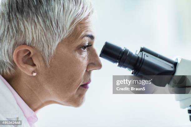 side view of a female scientist looking through a microscope. - scientist profile stock pictures, royalty-free photos & images