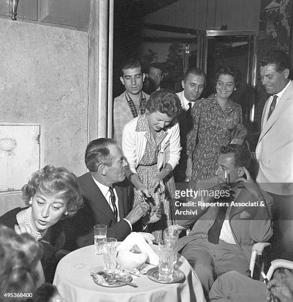 American actor Henry Fonda sitting at a table of the 'Casina delle rose' with his Italian wife Afdera Franchetti and signing an autograph for a fan....