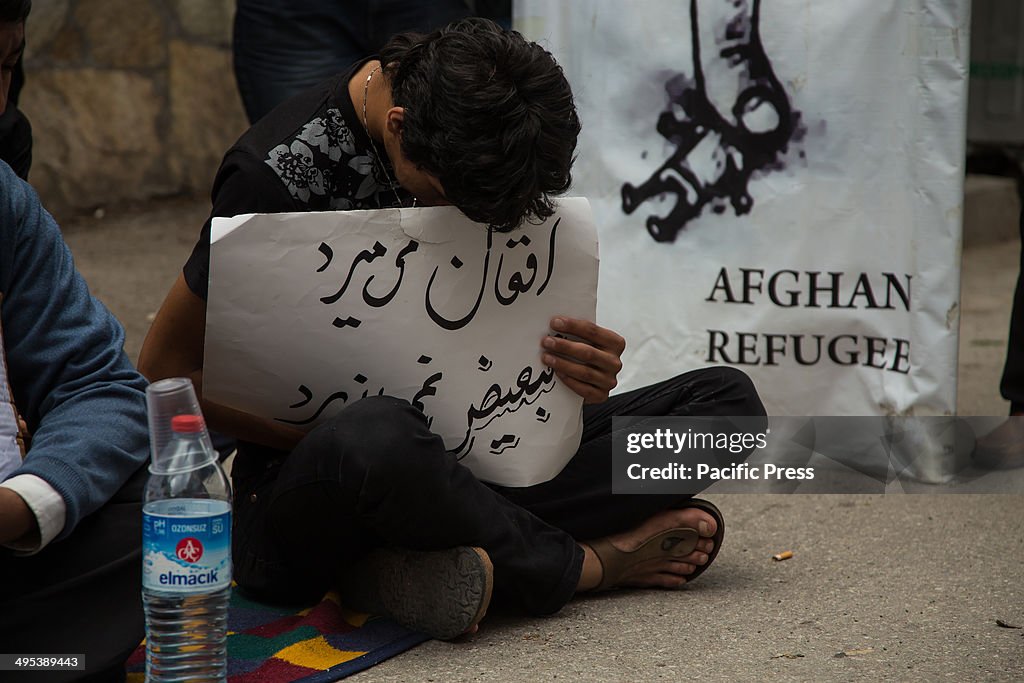 A young man holding a placard in Dari bows his head in...