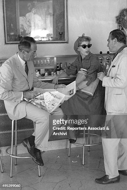 American actor Henry Fonda reading a newspaper beside his wife Afdera Franchetti talking to a man at the Doney bar on via Veneto. Rome, 1st August...