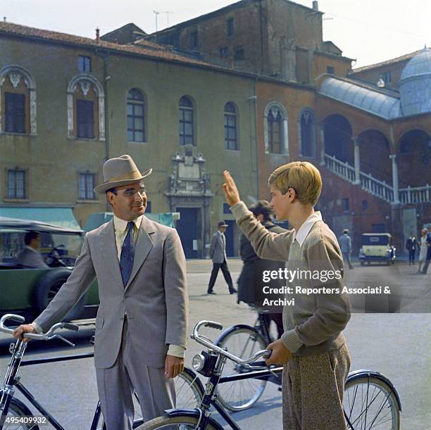 Two actors greeting each other holding a bicycle in a scene from the film The Garden of the Finzi-Continis. Italy, 1970