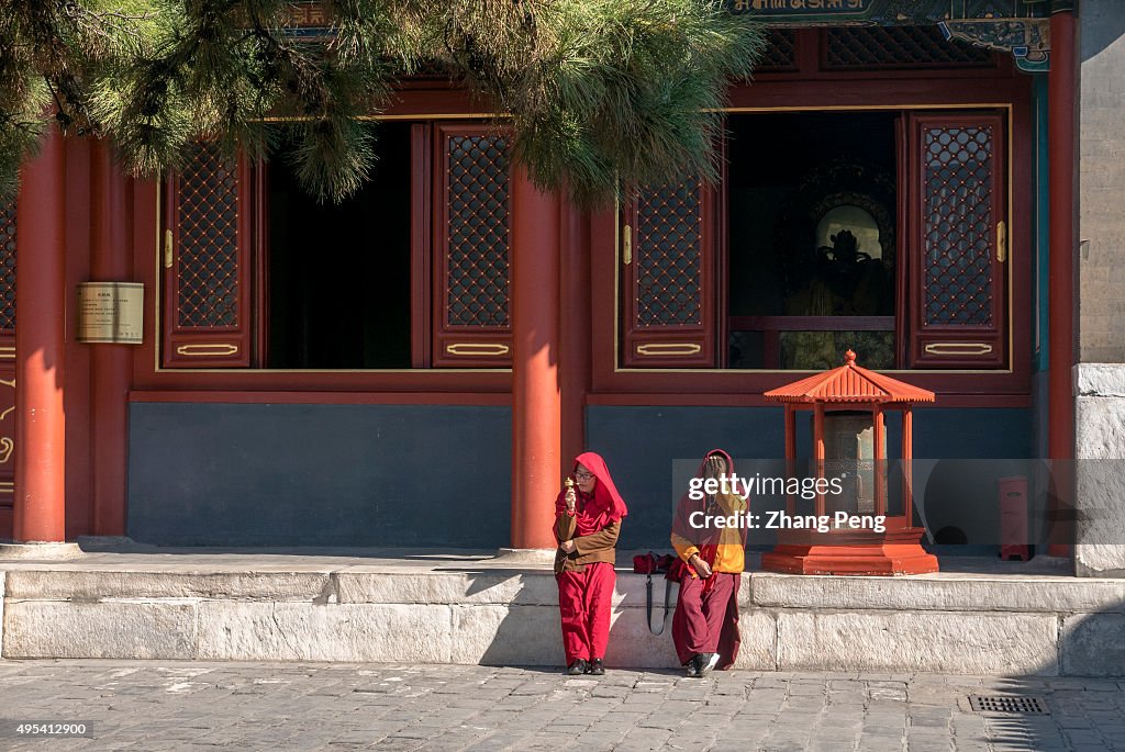 Tibetan monks rest beside a prayer wheel.  The Yonghe Temple...