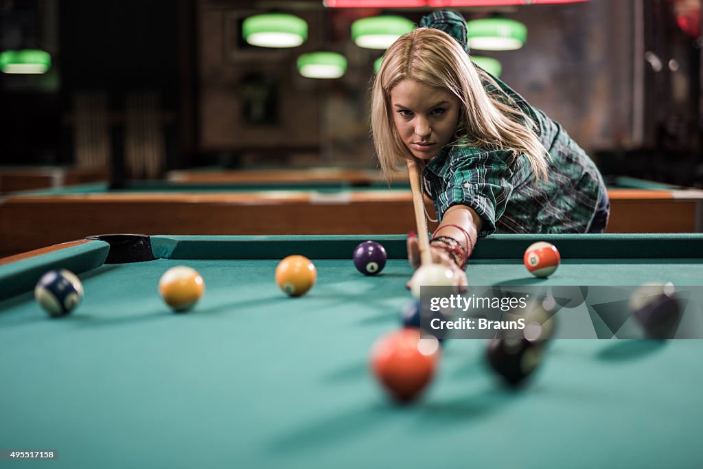 Young woman playing snooker in a pub.