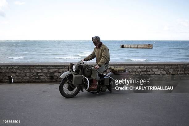 Man drives a vintage US Army Harley Davidson motorcycle as he passes a remain of the WWII "Mulberry harbour" in Arromanches-les-Bains, northwestern...