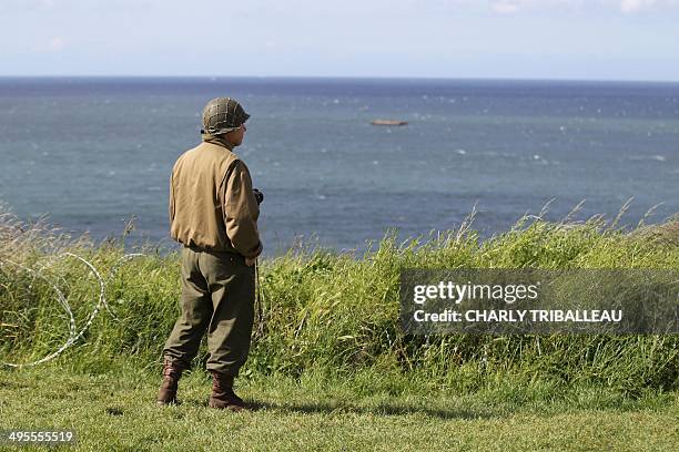 Man wearing a US World War II military uniform looks at the remains of the WWII "Mulberry harbour" on the beach of Arromanches-les-Bains,...