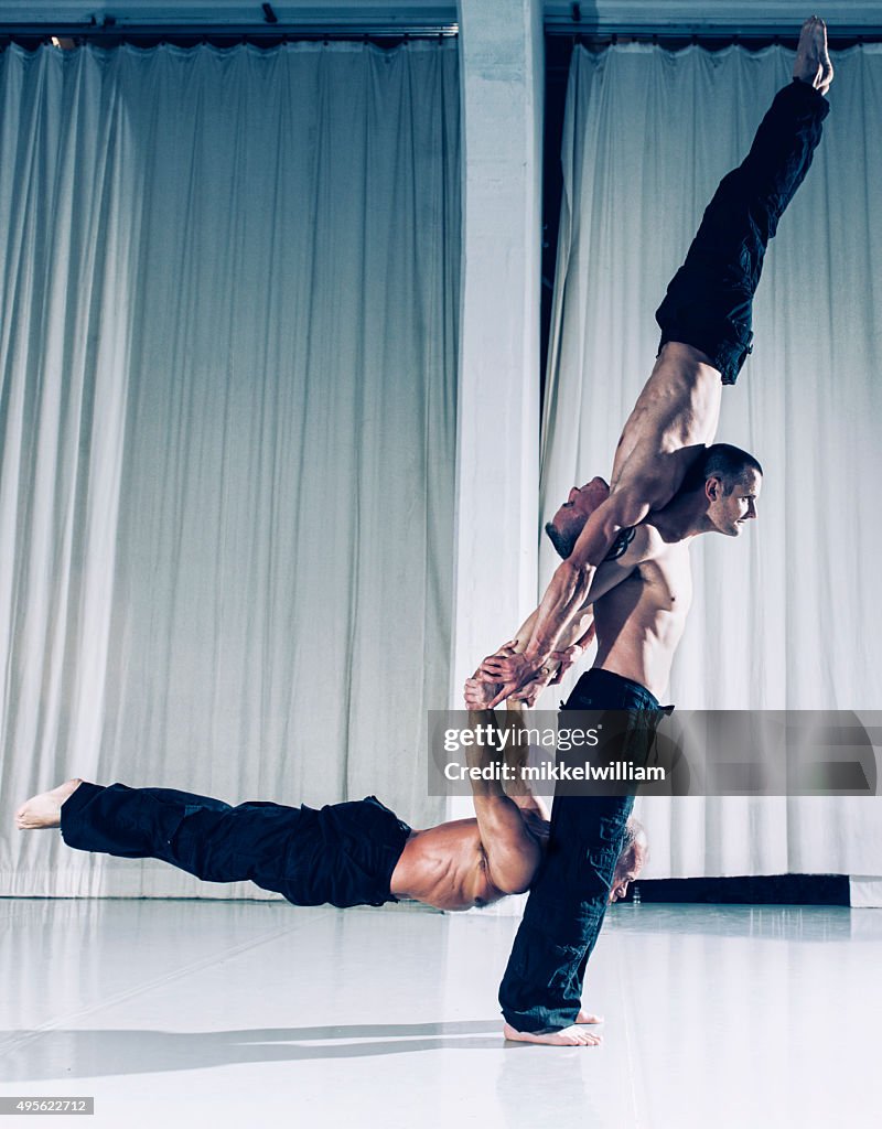 One strong acrobat holds two other men above the ground