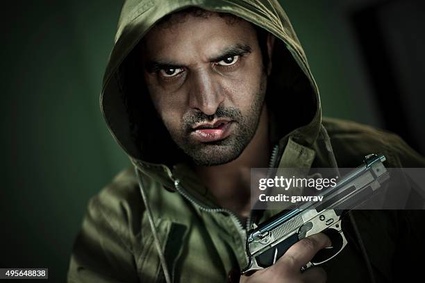 man in hoodie jacket with a gun and sharp gaze. - glaring meaning stock pictures, royalty-free photos & images