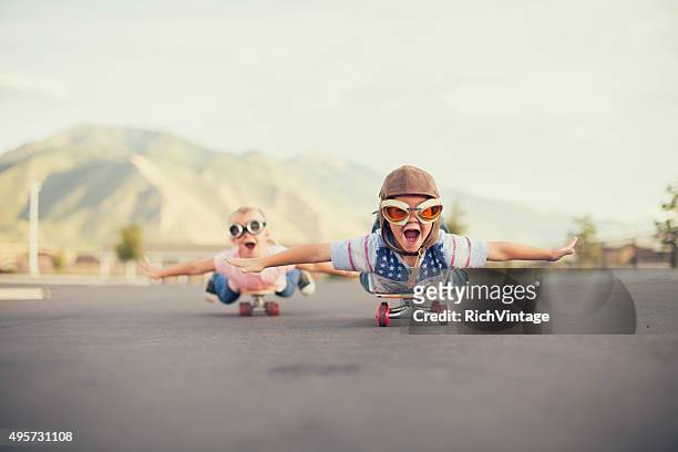 young boy and girl imagine volando sobre monopatín - creatividad fotografías e imágenes de stock