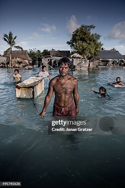 Family wading through the salty sea water that flooded their village. They float an old refrigerator after themselves as they collect seabed-stones...