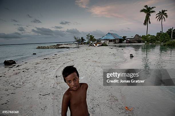 Young boy stands on a narrow strip of land that luckily didn't flood and prevented his home from being drowned in the sea with the village Eita. The...