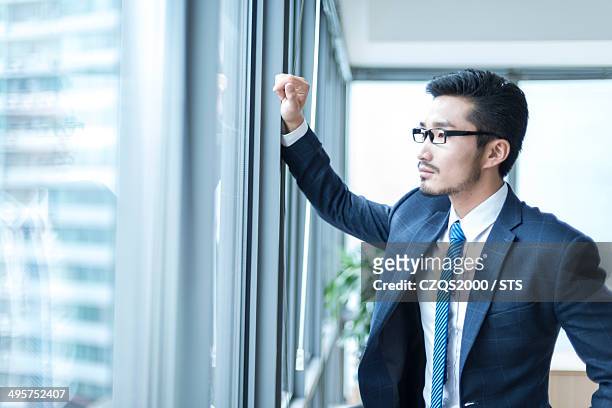businessman looking out of office window - portrait of pensive young businessman wearing glasses stock-fotos und bilder