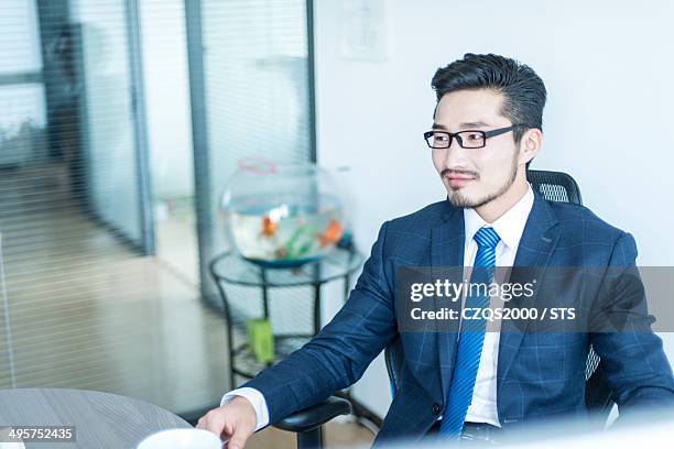 businessman seated in office - portrait of pensive young businessman wearing glasses stock-fotos und bilder