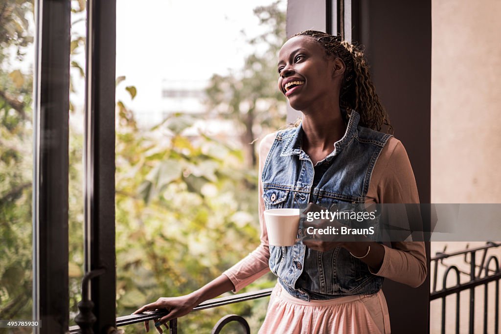 Heureuse femme afro-américaine avec une tasse de café sur la terrasse.