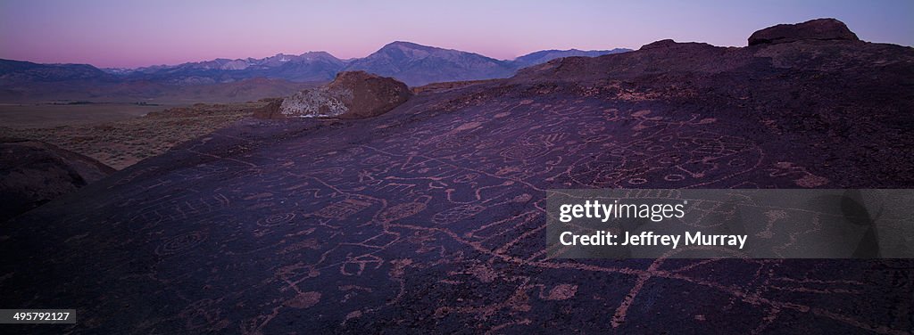 Sky Rock petroglyphs near Bishop, California, during sunset with the Sierra Nevada mountain range in the distance.