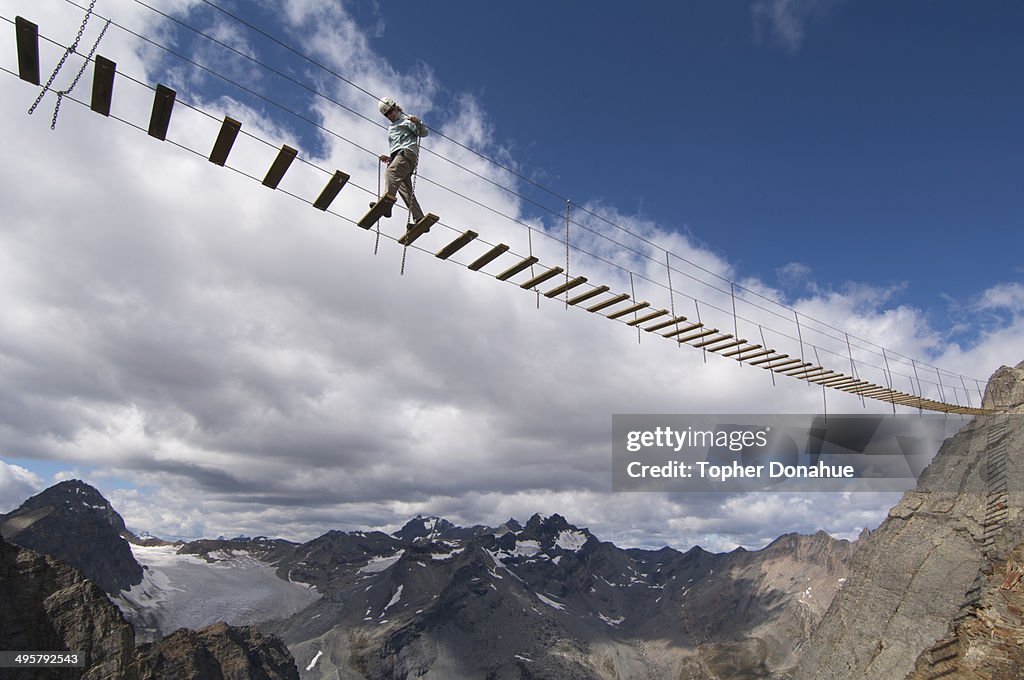 A woman crosses an exposed suspension bridge.