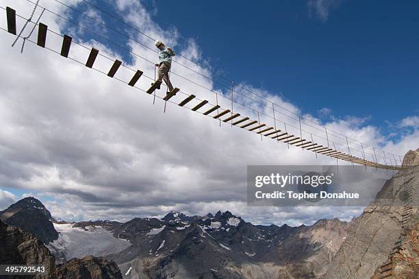 a woman crosses an exposed suspension bridge. - touwbrug stockfoto's en -beelden