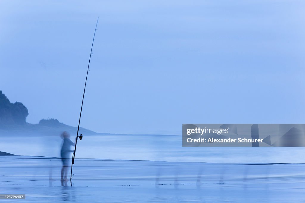 Child on beach with a fishing rod at dusk, Oakura, Taranaki Region, New Zealand