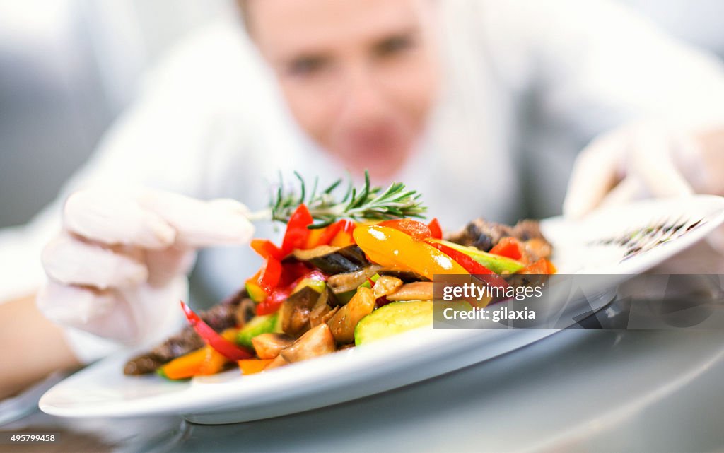 Female chef places finishing touches on meal.