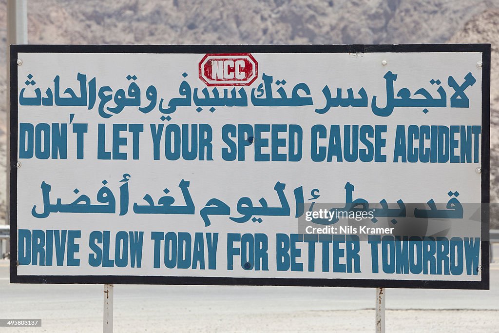 Bilingual grammatically wrong road sign in Arabic and English Do not let your speed cause accident, drive slow today for better tomorrow, Oman