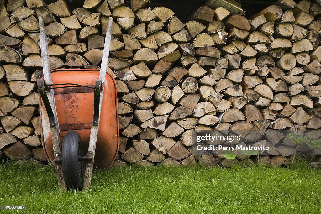 Orange wheelbarrow propped up against stacked firewood, Quebec City, Quebec Province, Canada