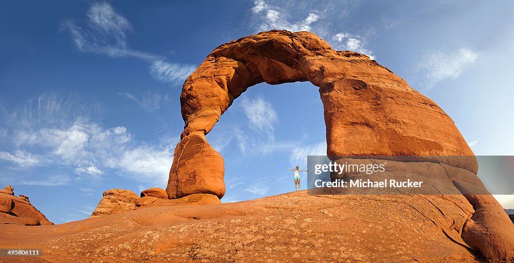 Woman standing under Delicate Arch natural stone arch, Arches-Nationalpark, near Moab, Utah, United States