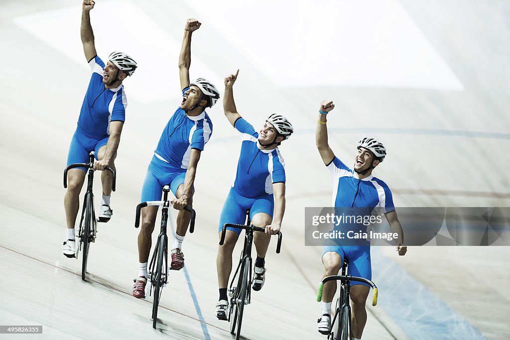 Track cycling team riding in velodrome with arms raised