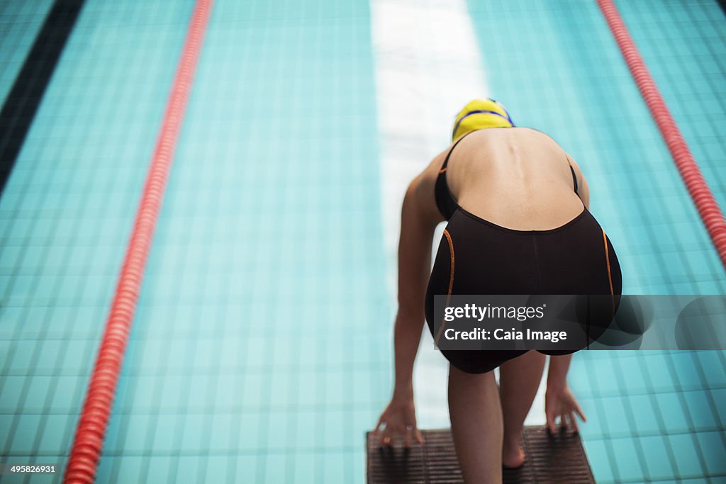 Swimmer poised at starting block above pool