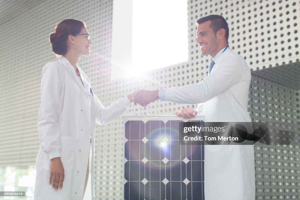 Scientists handshaking at solar panel in laboratory