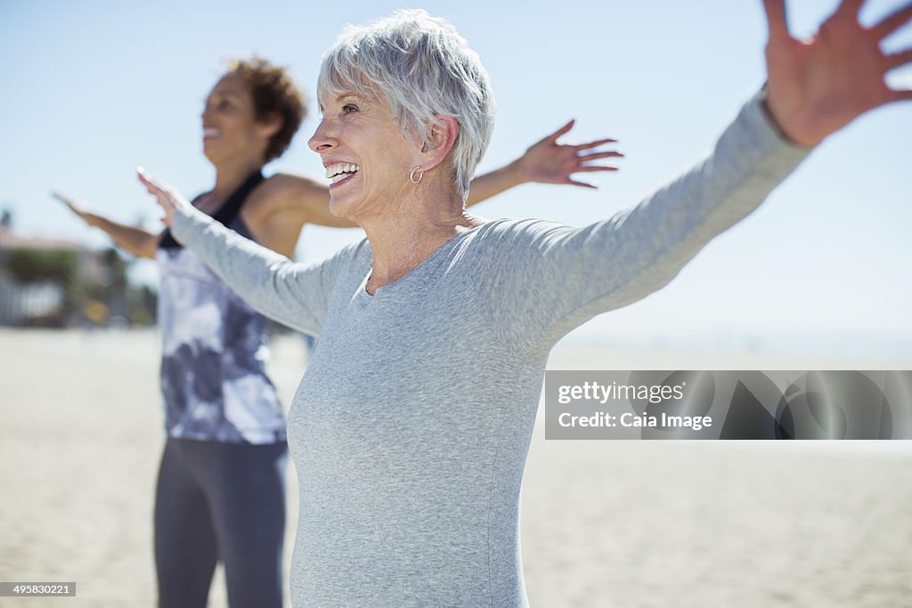 Senior women stretching arms on beach