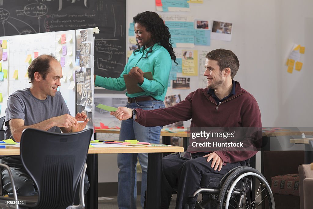 Engineering instructor reviewing technical material with students in ideation lab, one man with spinal cord injury and other one with Aspergers